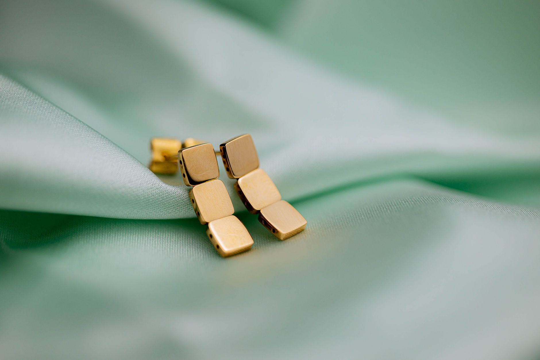 Conceptual gold earrings resting on green satin